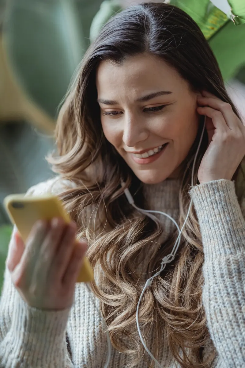 Vrouw met oortjes kijkt glimlachend naar haar telefoon